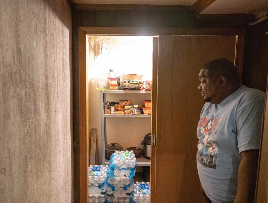 Cleophus Mooney, at the right of the frame, looks at 8 cases of bottled water he has stored in a closet in his home in Flint, Michigan, on Oct. 22, 2020