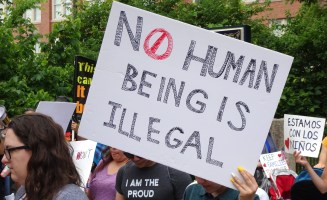 a person holds a square sign that reads No Human Being is Illegal at a protest
