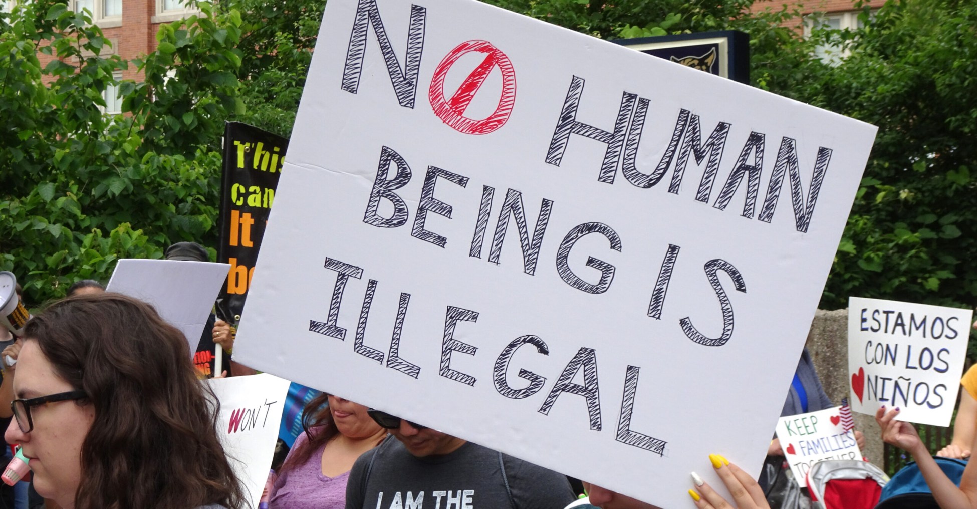 a person holds a square sign that reads No Human Being is Illegal at a protest