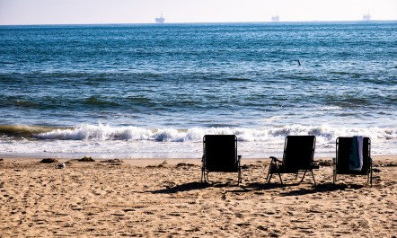 Three empty beach chairs on a beach in Southern California, and 3 oil drilling rigs—ominous in the distance