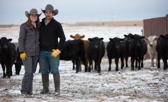 Kelsey Scott and Monte Scott pose together in front of a herd of cattle.