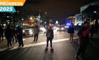 A night-time image of several protesters standing in a street as headlights in the distance illuminate them.