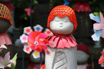 a statue in Japan shows a small stone person with a red hat and a flower
