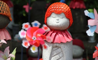 a statue in Japan shows a small stone person with a red hat and a flower
