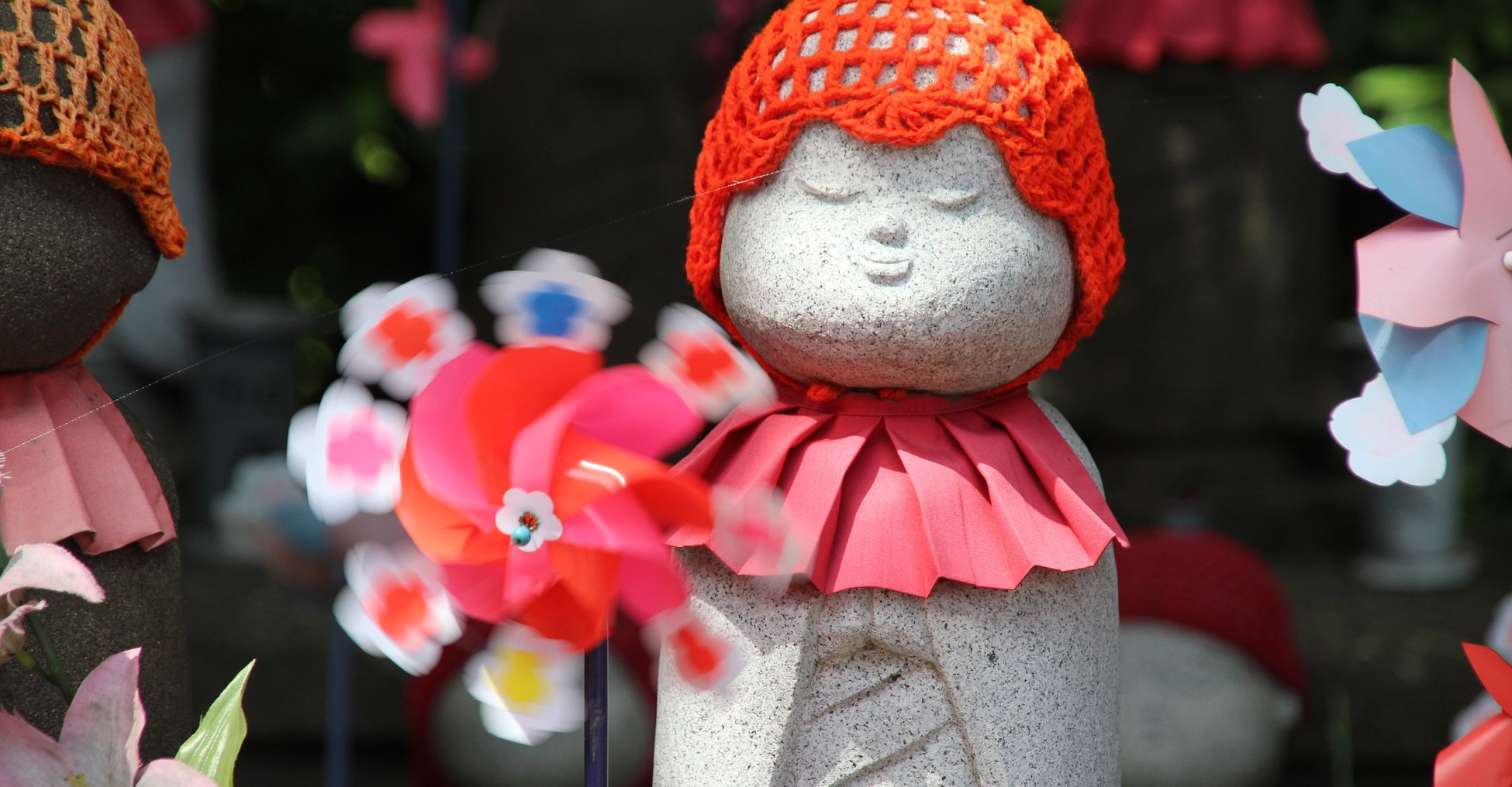 a statue in Japan shows a small stone person with a red hat and a flower